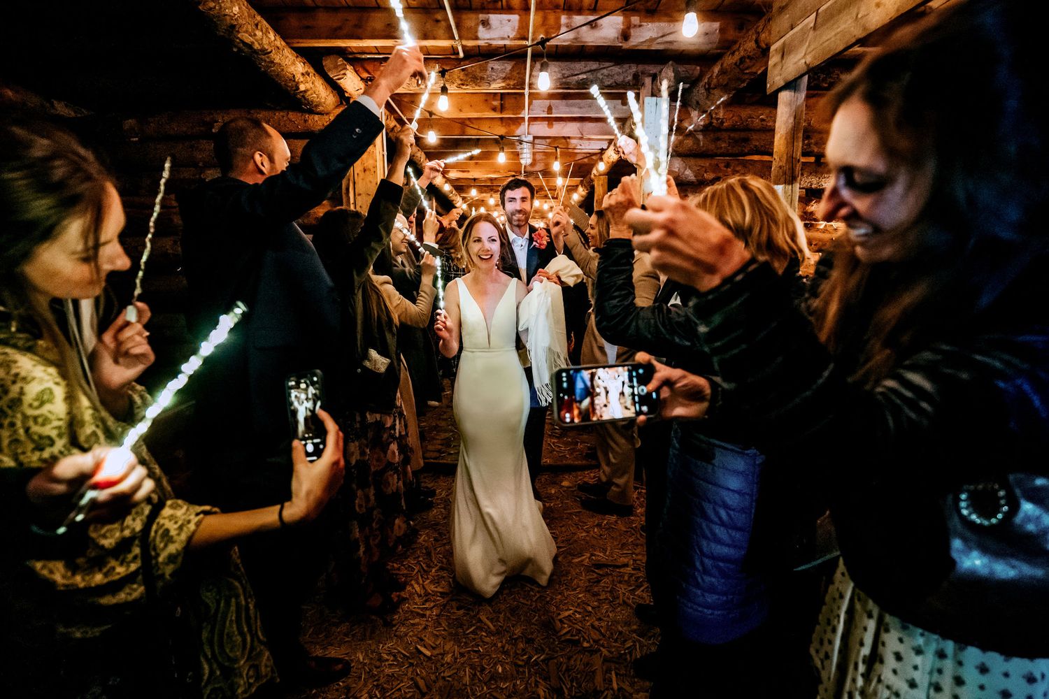 Party guests hold glowing wands to create a magical walkway for a bride in white.