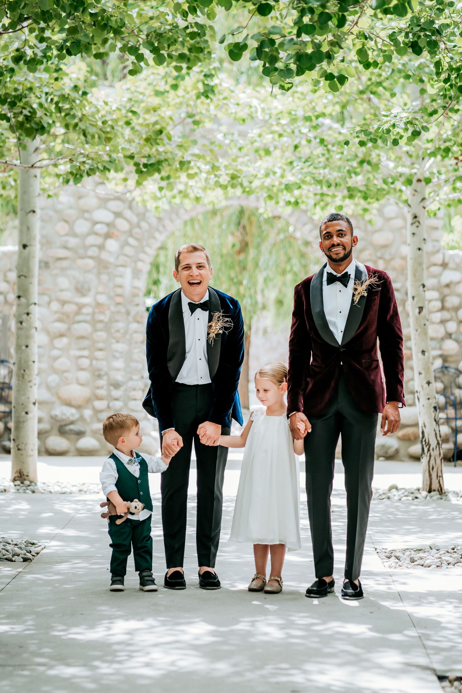 Wedding portrait with children beneath canopy of green leaves and stone archway.