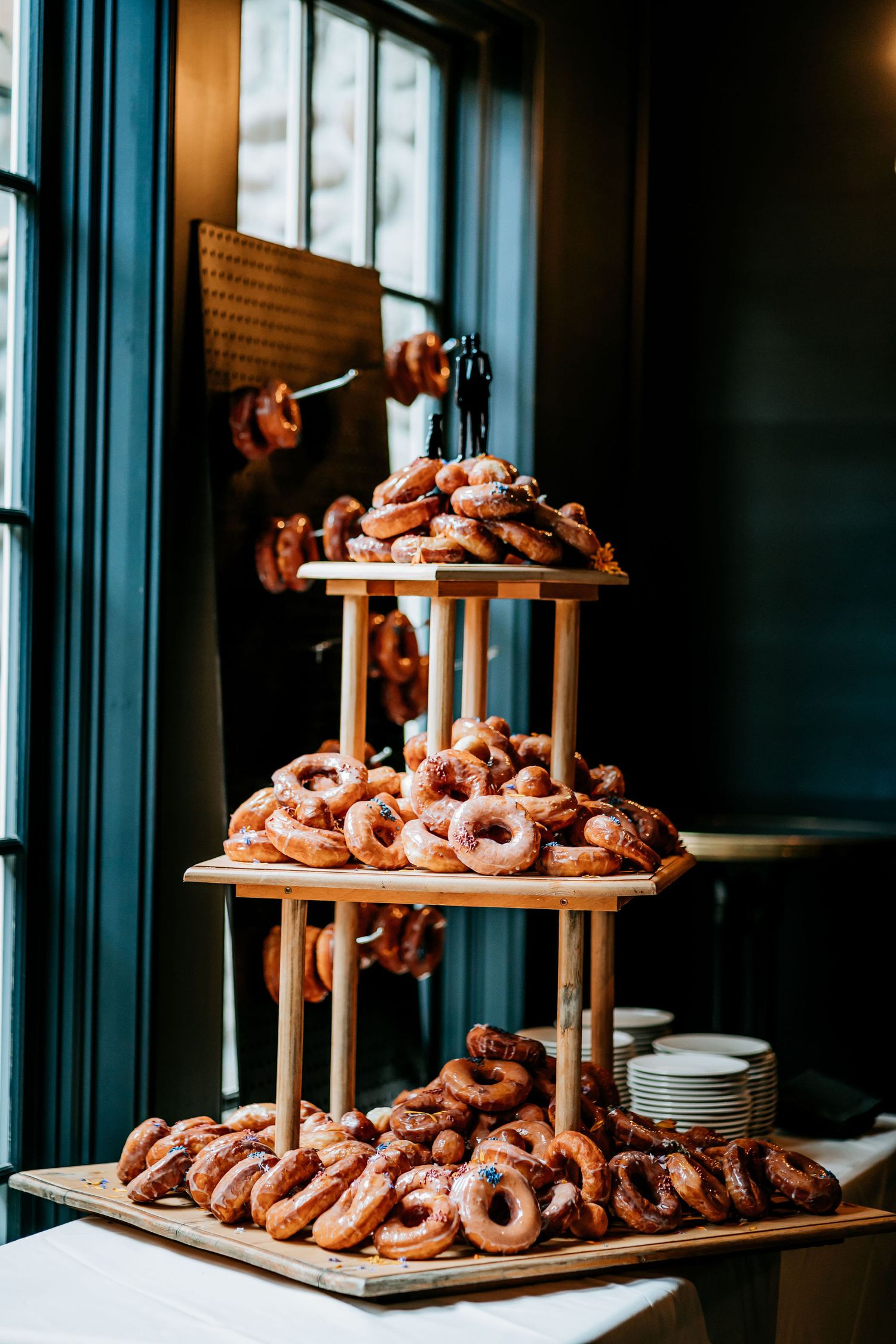 Three-tiered wooden display stand filled with fresh donuts at an elegant event.