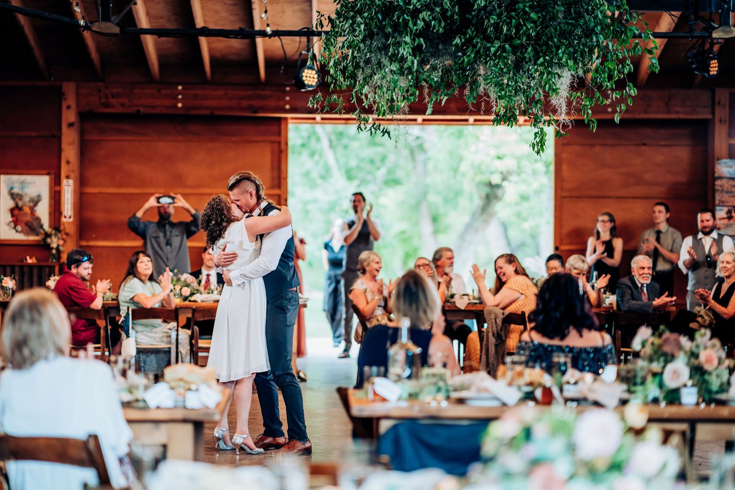 Wedding celebration in a rustic venue with hanging plants and a green backdrop display.