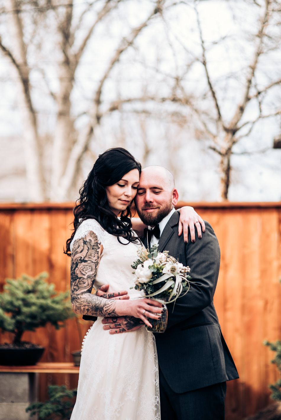 Intimate wedding portrait with couple embracing against wooden fence backdrop.
