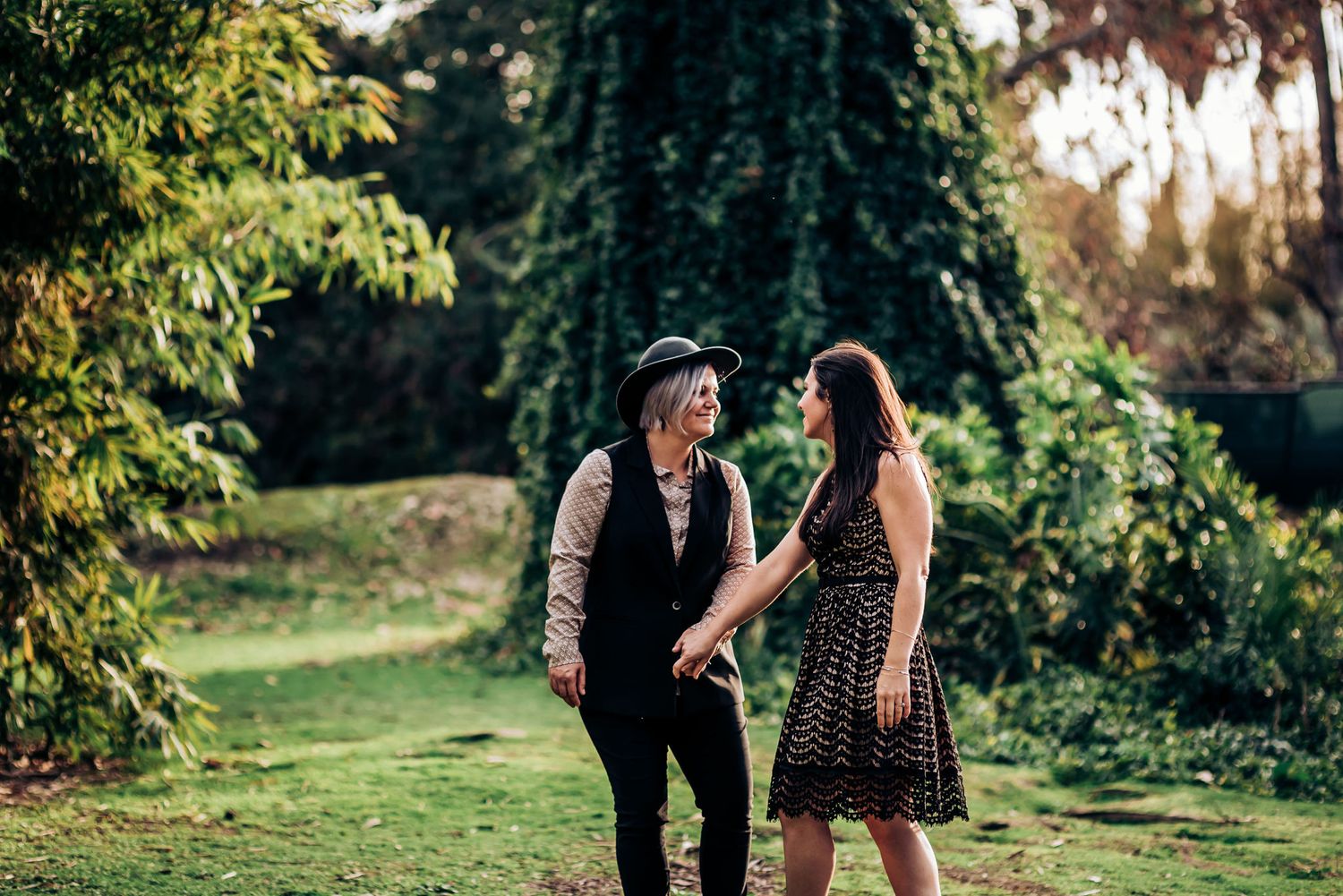 Two people share a tender moment in a garden with sunlit trees.