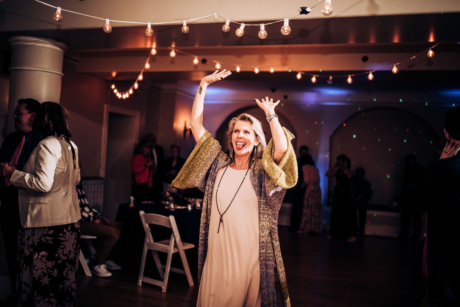 Guest dancing enthusiastically at indoor party venue with string lights and ambient lighting.