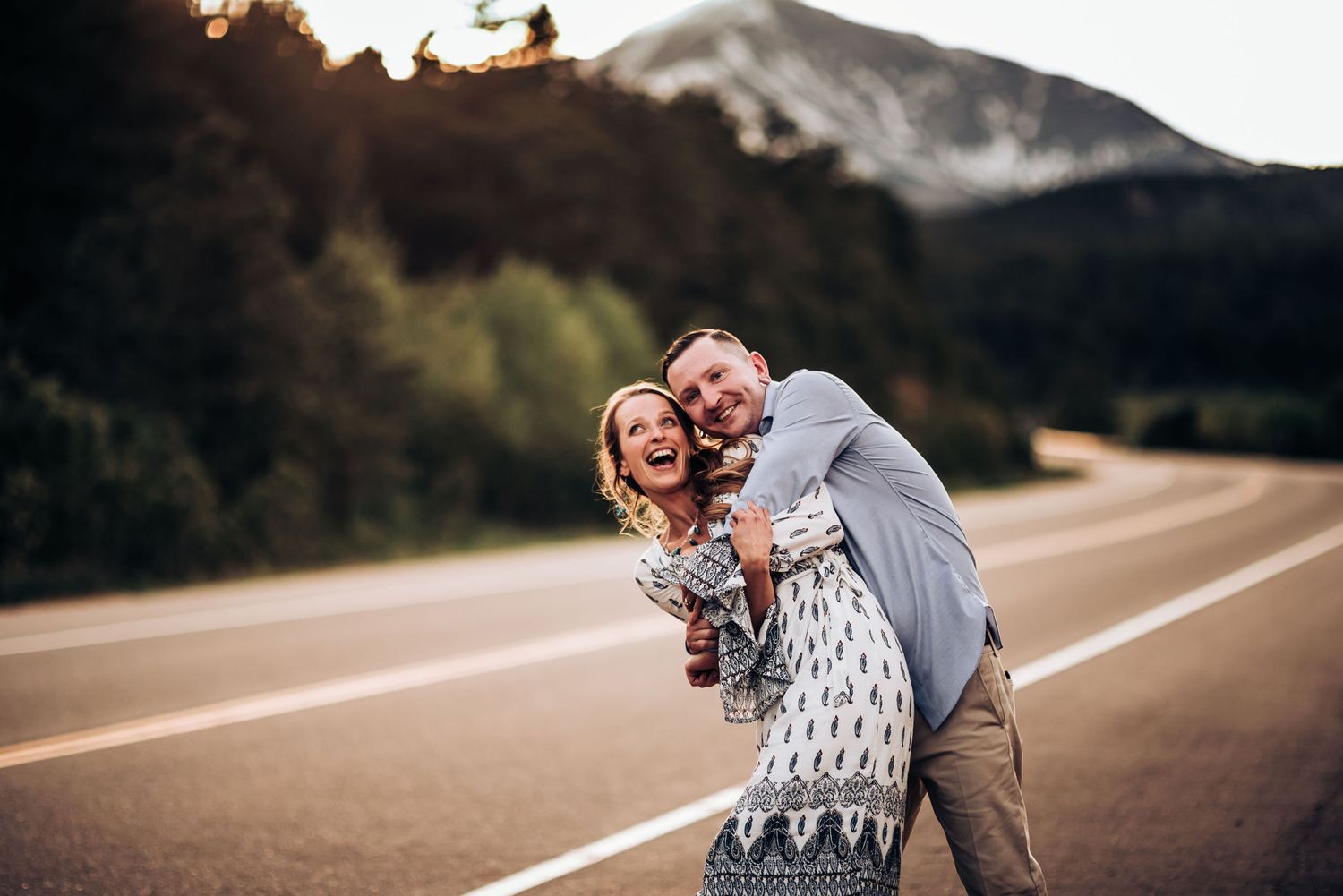 Playful couple laughing together on mountain road with scenic backdrop.