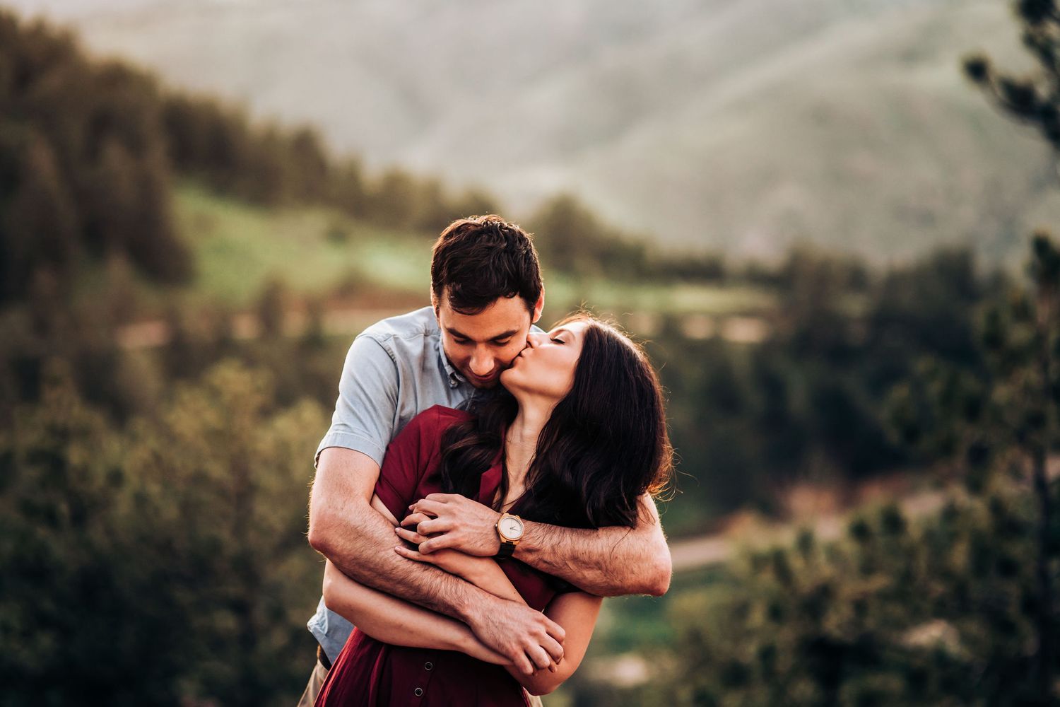 Romantic embrace captured against mountain backdrop during outdoor photoshoot.