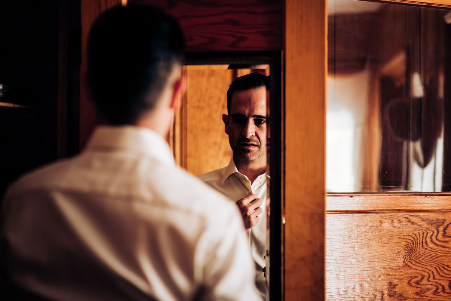 Reflection of person adjusting tie in wooden framed mirror.