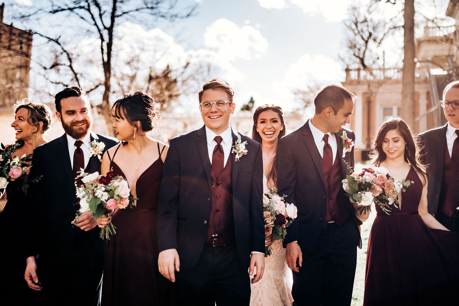 Wedding party in formal attire stands together outside on sunny winter day.