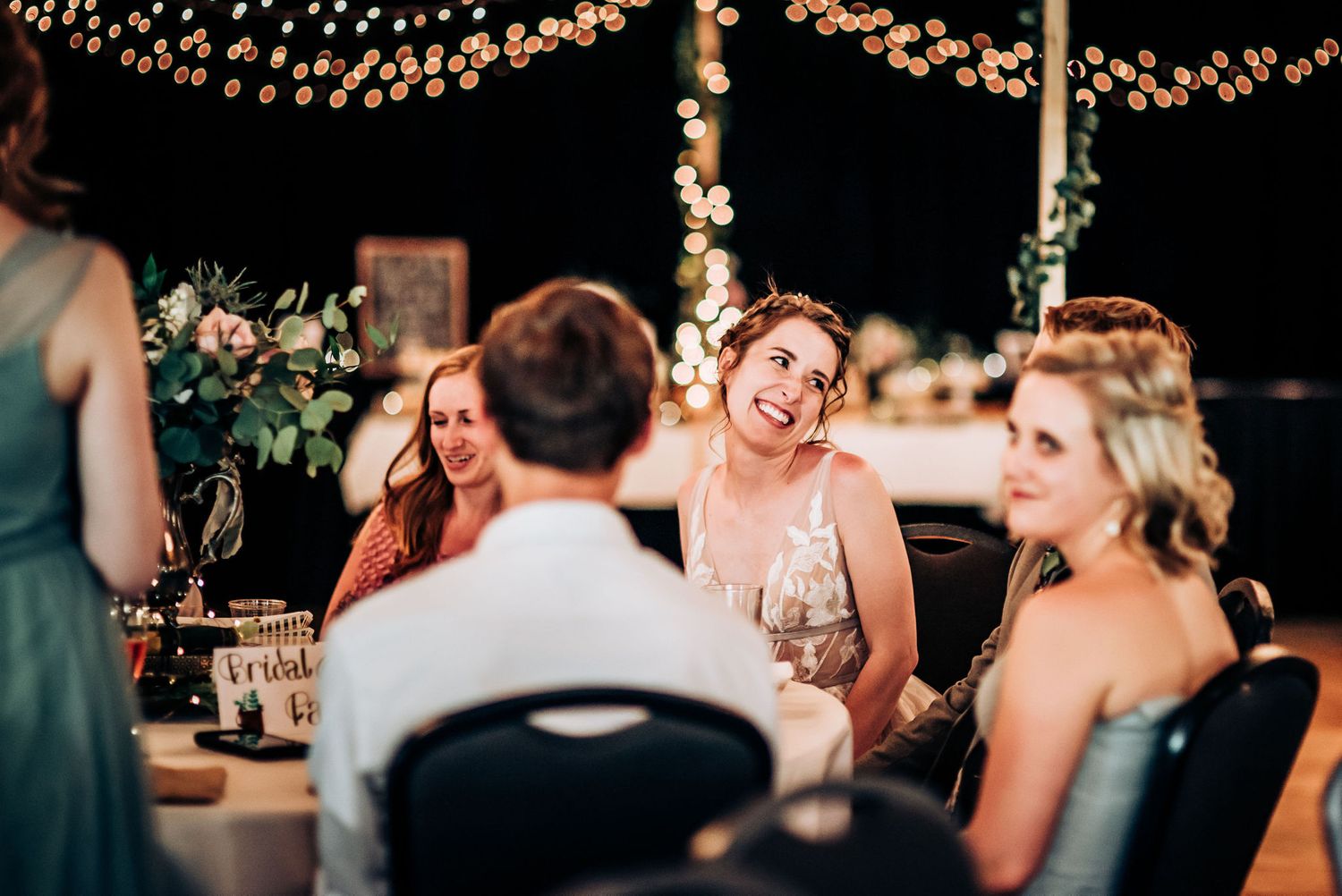 Wedding reception dinner party under twinkle lights with guests enjoying conversation.
