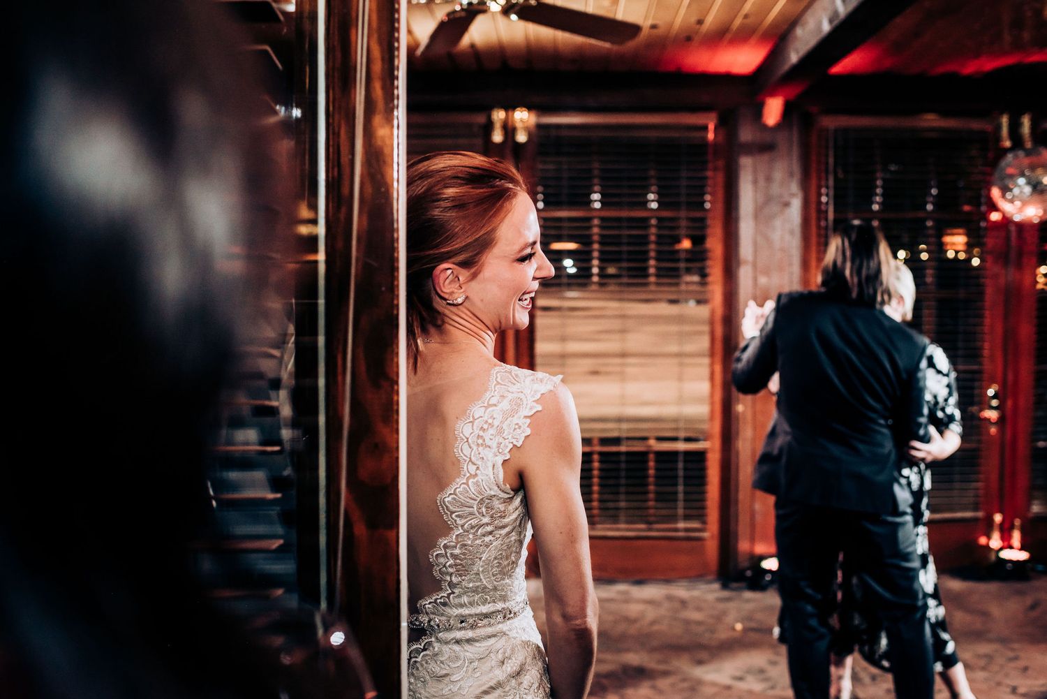 Elegant bride in a sparkly dress stands in a rustic wooden venue during reception.
