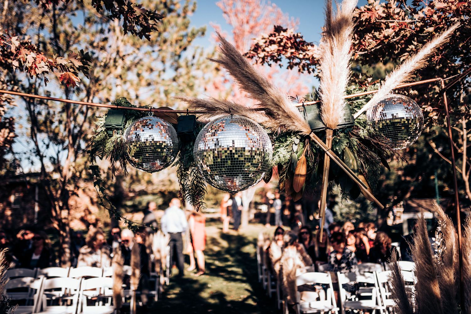 Outdoor wedding ceremony setup with white chairs under trees and natural lighting filtering through branches.