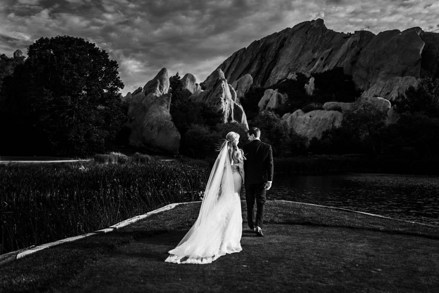 Dramatic black and white wedding photo with couple standing before majestic mountain landscape.