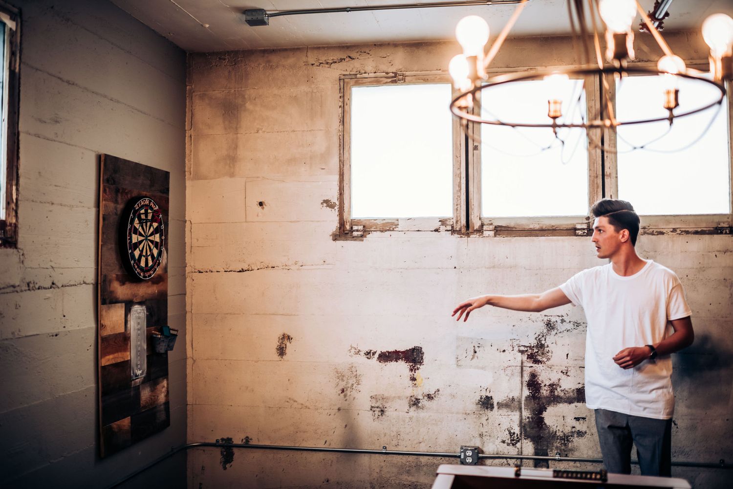 Person playing darts in an industrial room with exposed walls and vintage lighting.