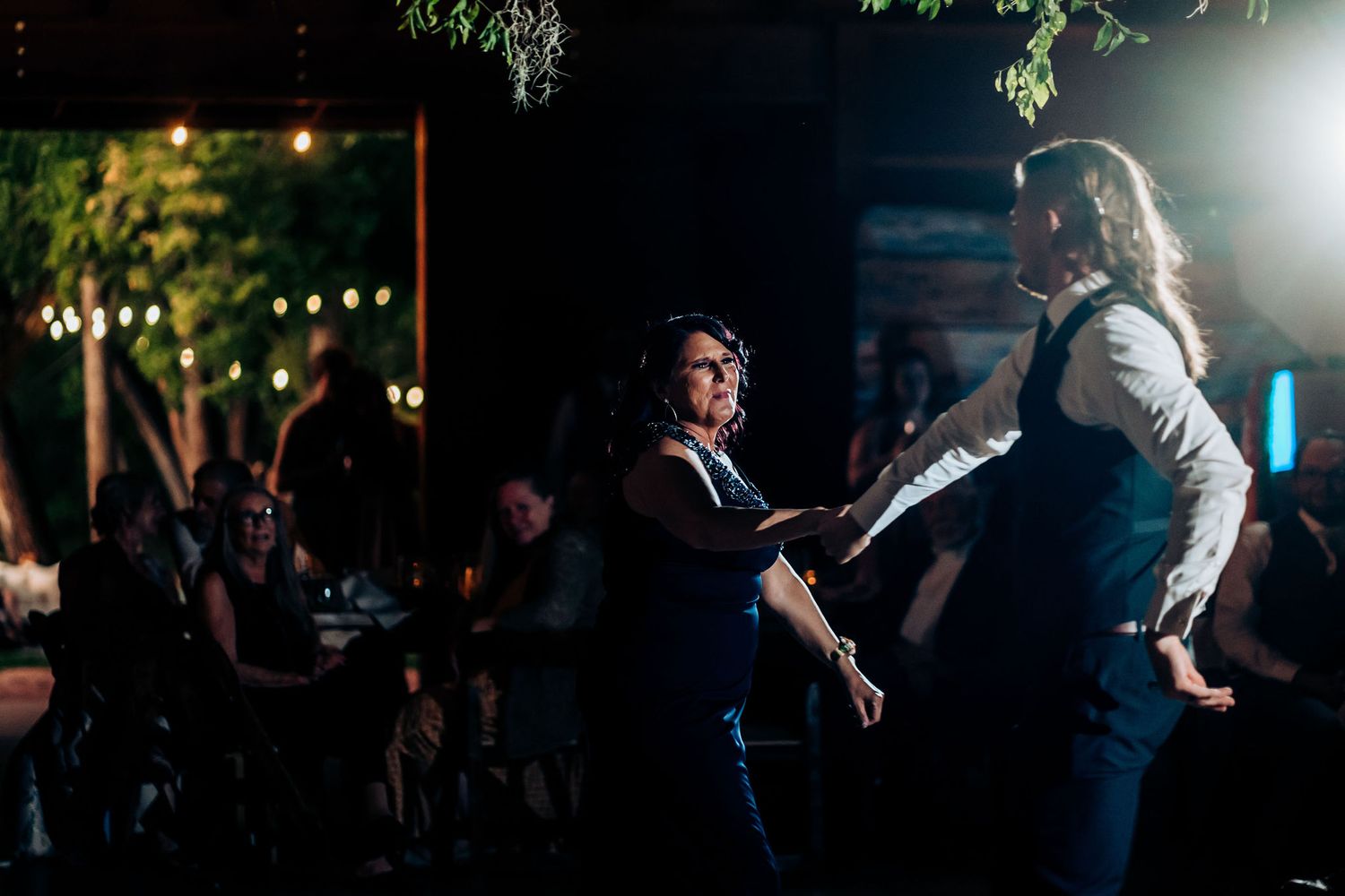 Couples dance together during an evening celebration in a dimly lit venue with string lights overhead.