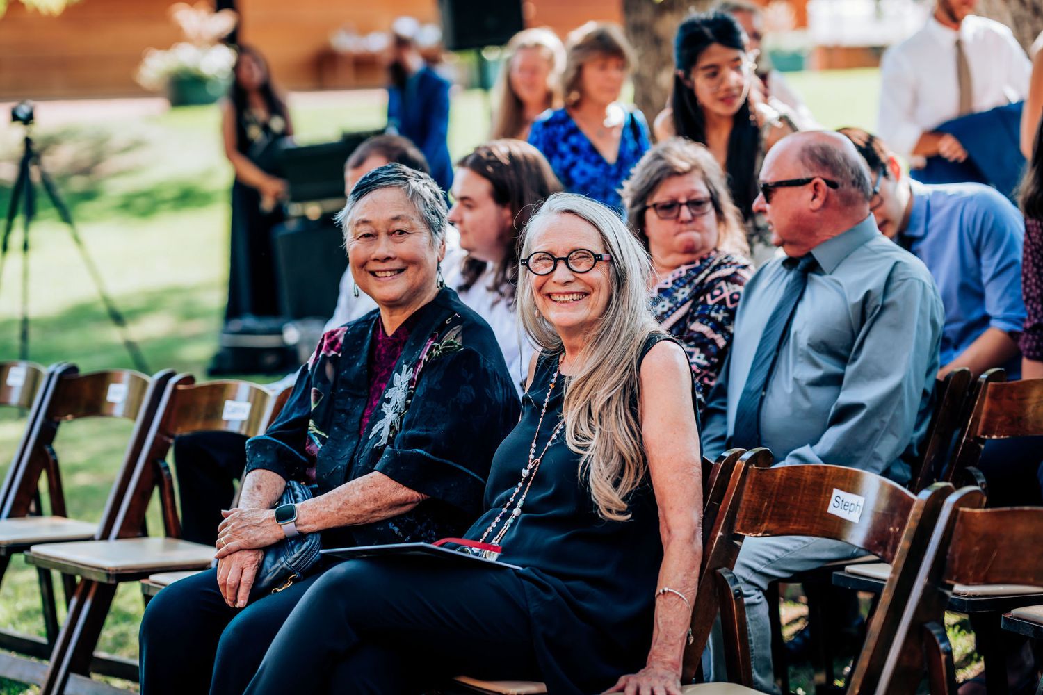 Wedding guests seated in rows of wooden chairs during an outdoor ceremony.