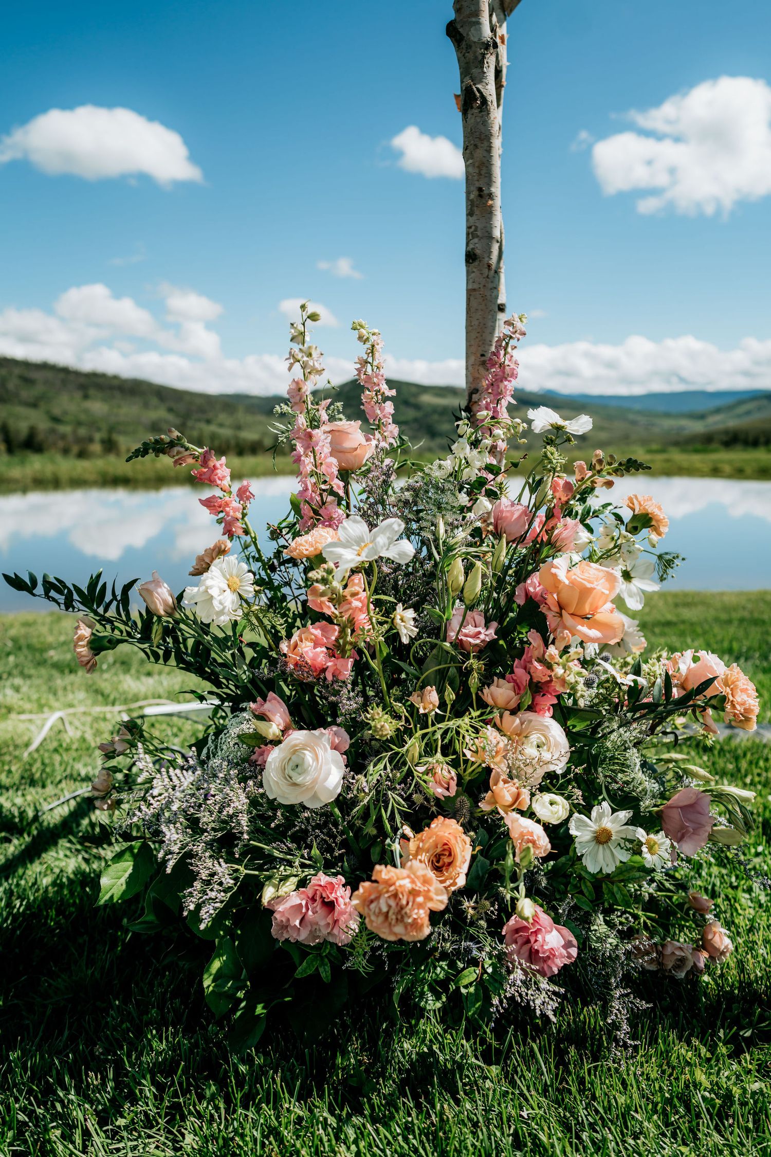 Stunning floral arrangement with pink and peach roses against a mountain lake backdrop.