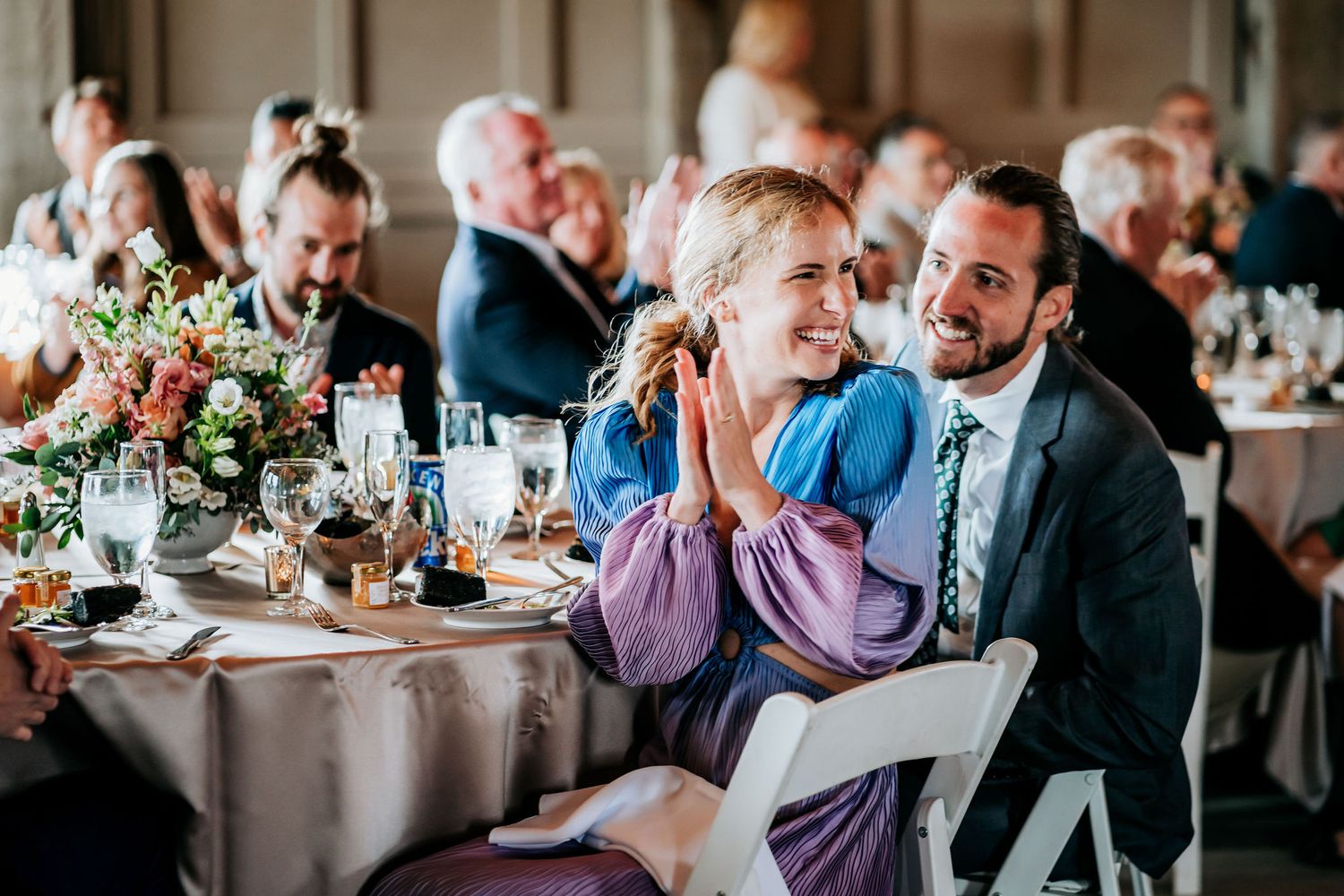 Wedding guests share emotional reactions during reception speeches at decorated tables.