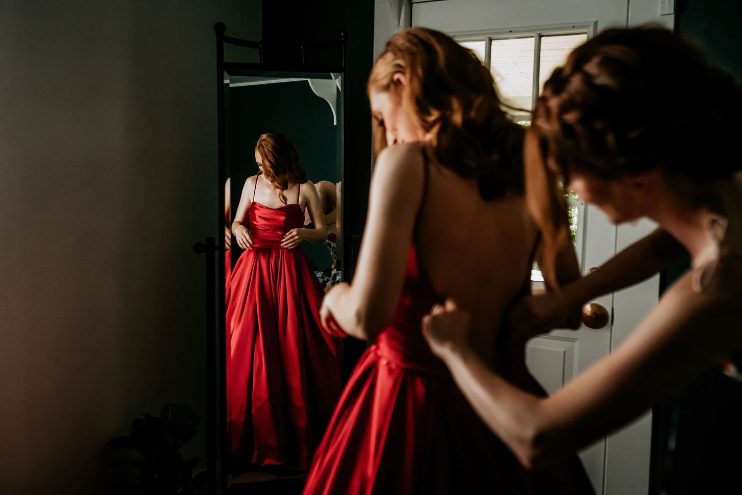 Getting ready scene with red formal dress reflected in mirror during special event preparations.