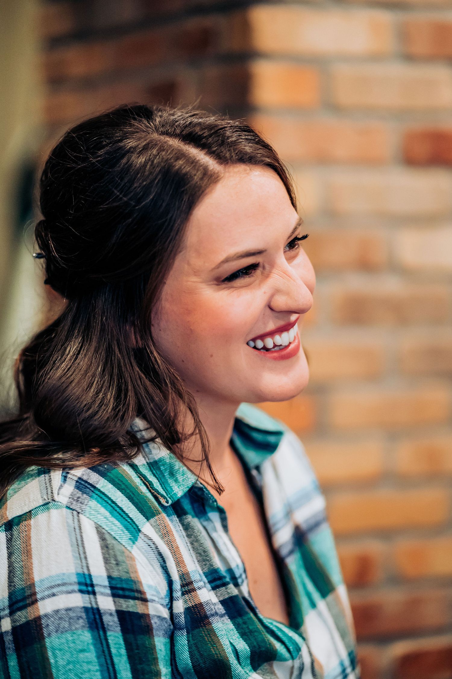 Candid moment during makeup preparation against exposed brick wall.