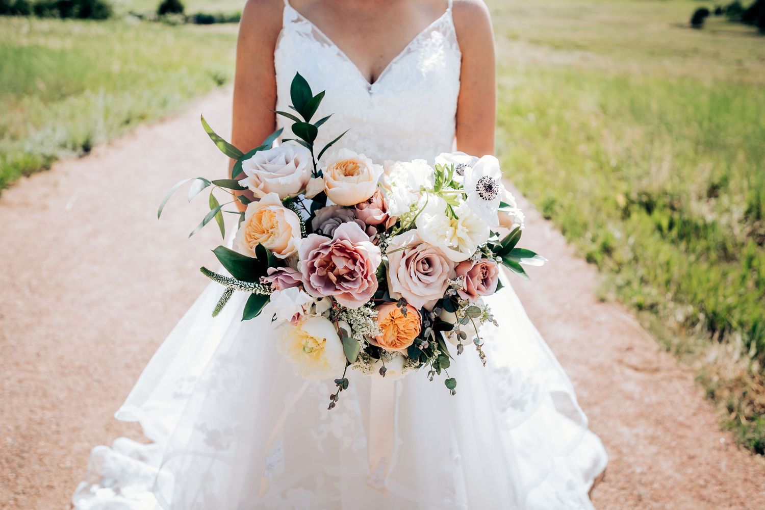 A bridal bouquet featuring pink and peach roses against a white wedding dress.