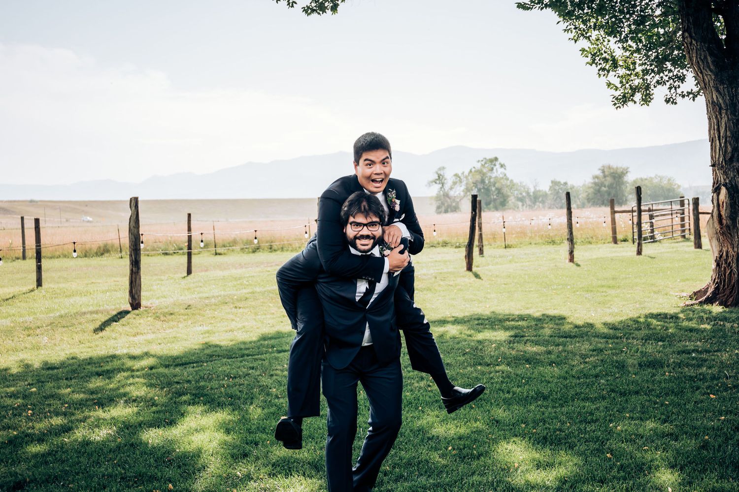 Playful moment captured between couple in formal attire on grassy hill with mountain backdrop.