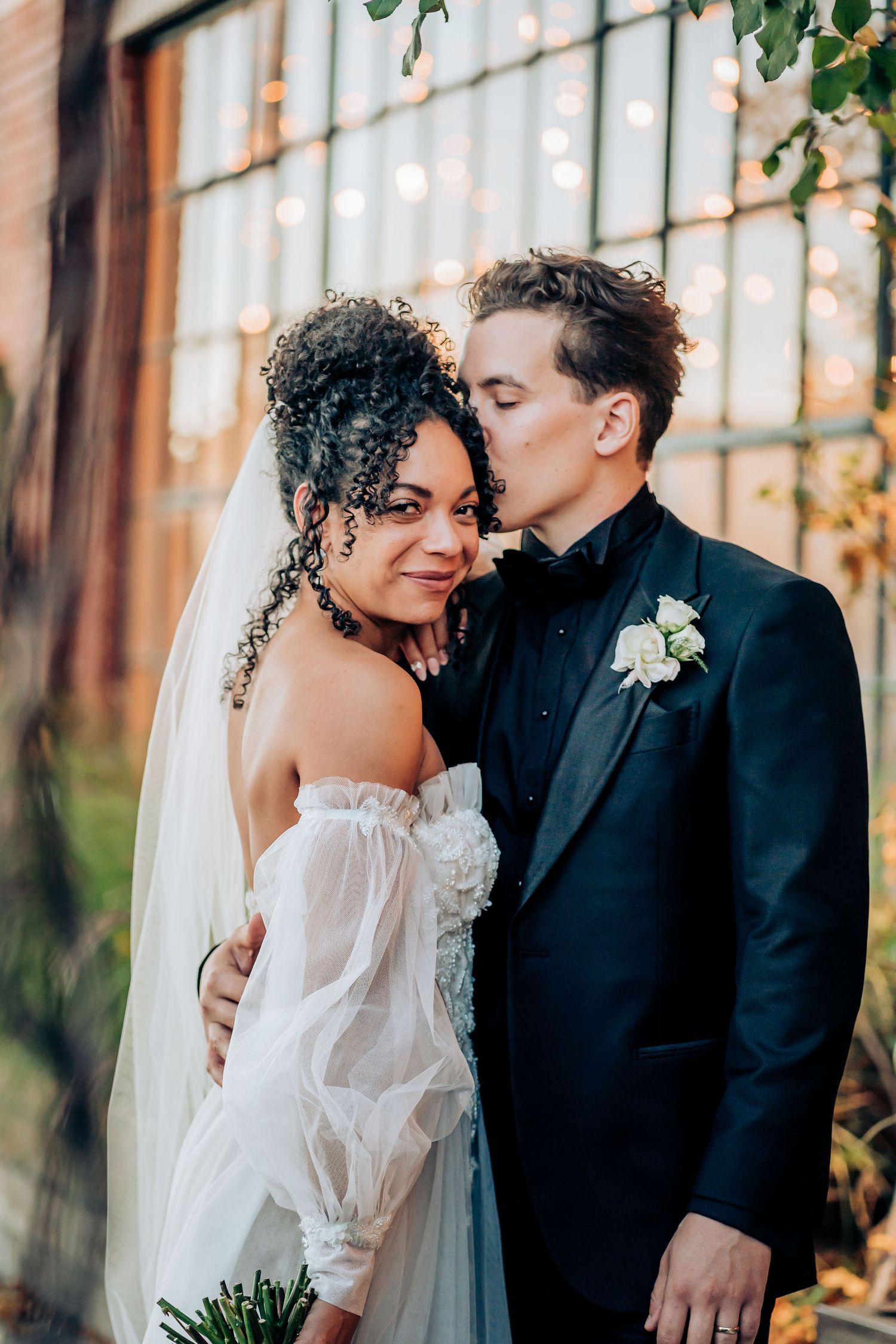 An intimate wedding portrait captured against industrial windows with warm lighting.