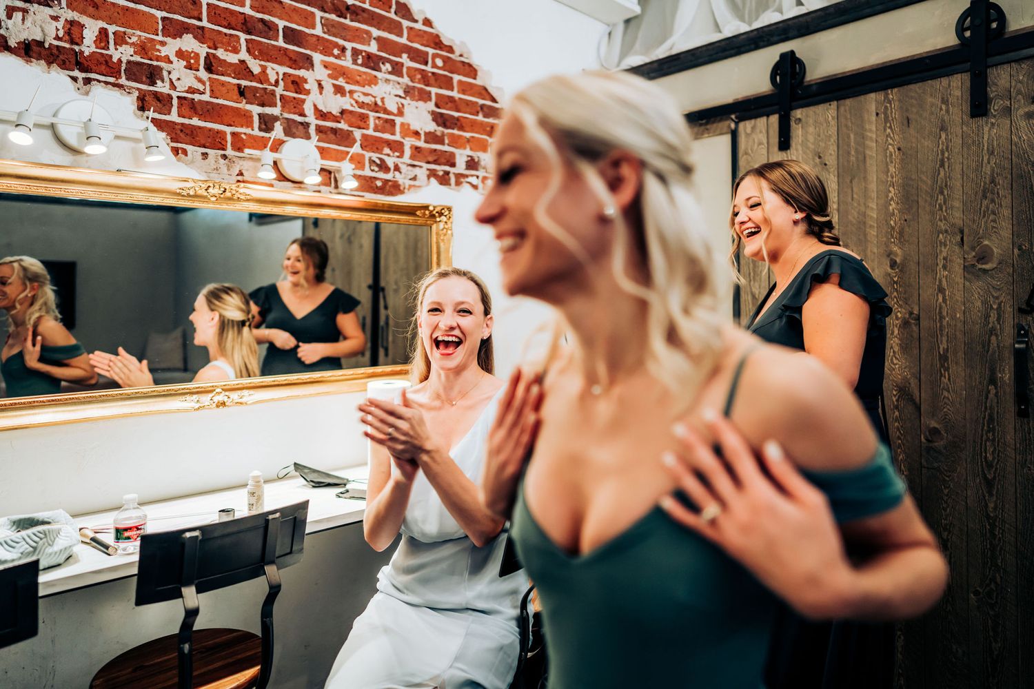 Joyful reactions and laughter in a dressing room with exposed brick walls and mirrors.