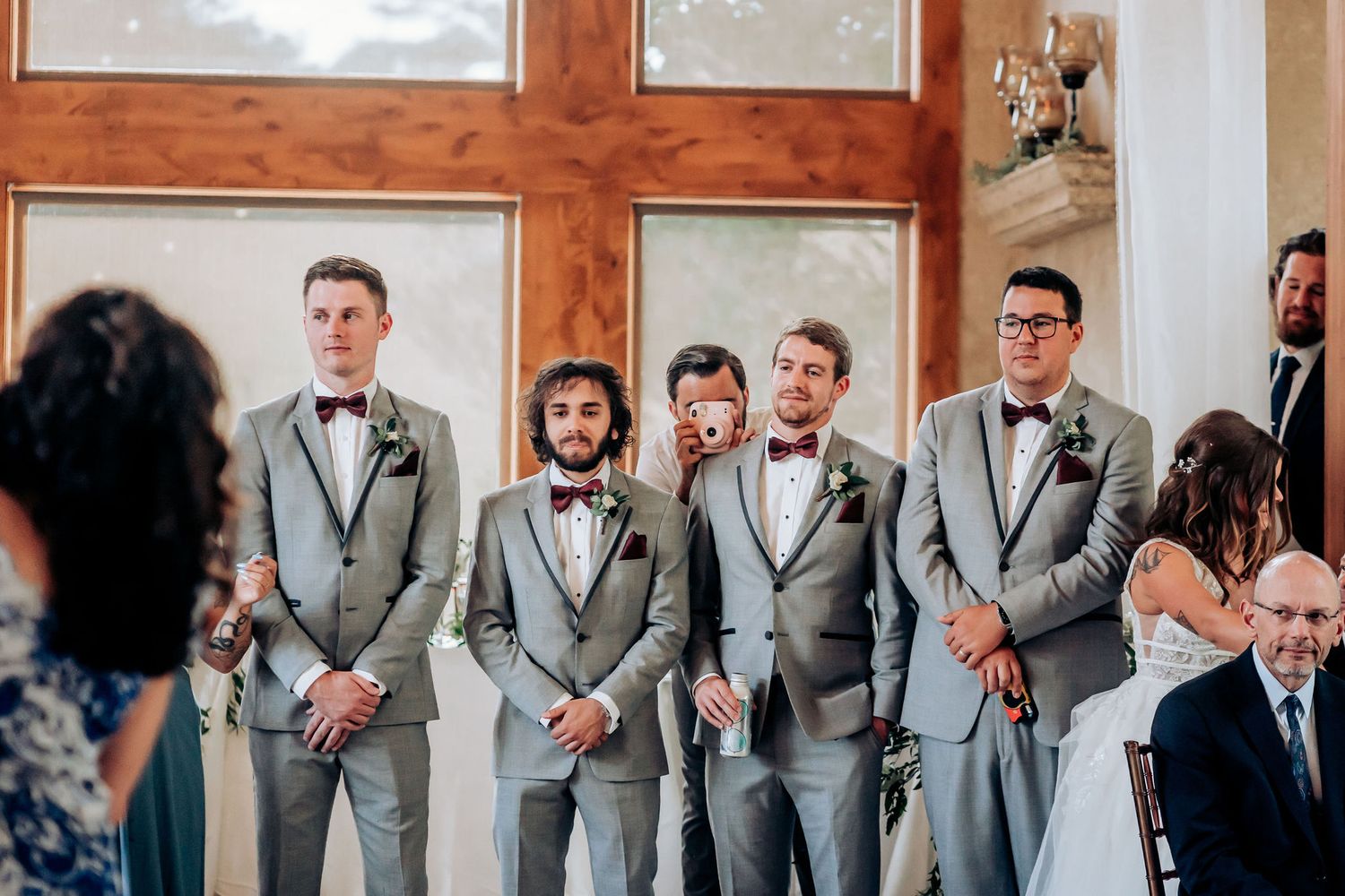 Groomsmen in matching gray suits and bowties stand attentively during a wedding ceremony.