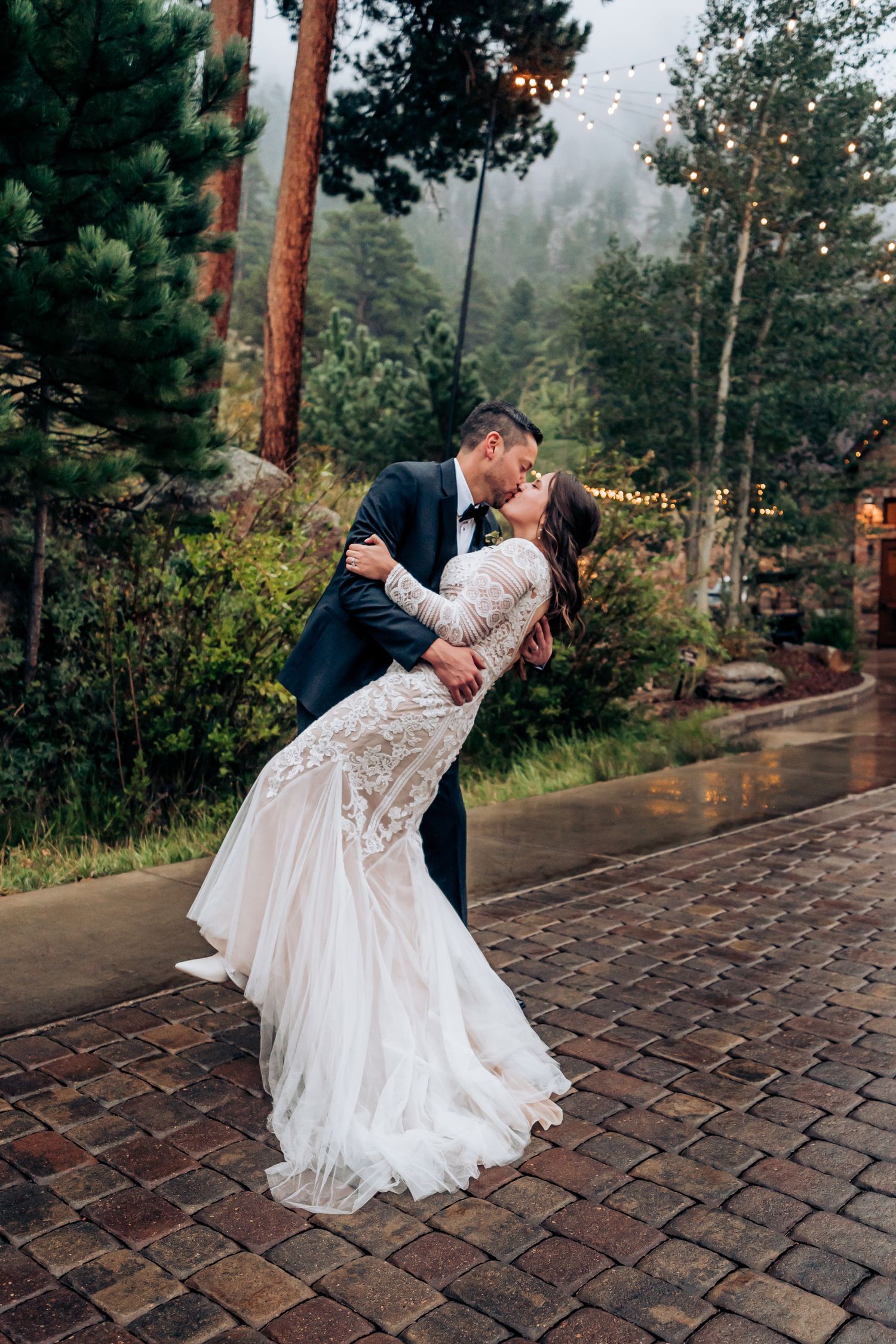Romantic dip pose on brick patio with elegant lace wedding dress flowing.