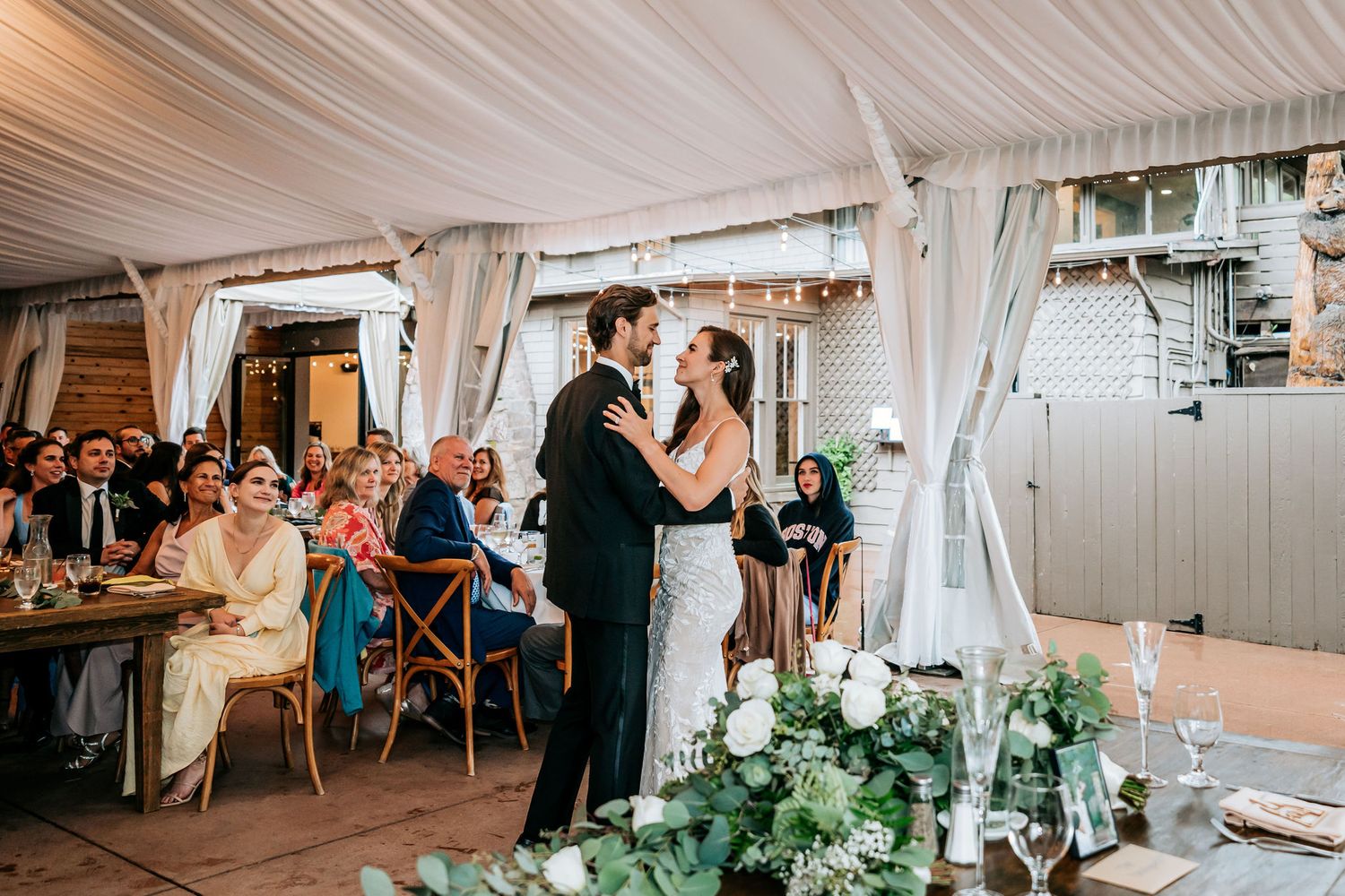 Wedding reception under draped white tent with floral centerpieces and string lights.
