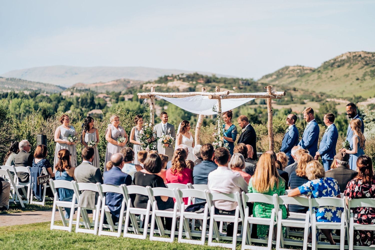 Outdoor wedding ceremony with mountain views and white chairs under bright blue sky.