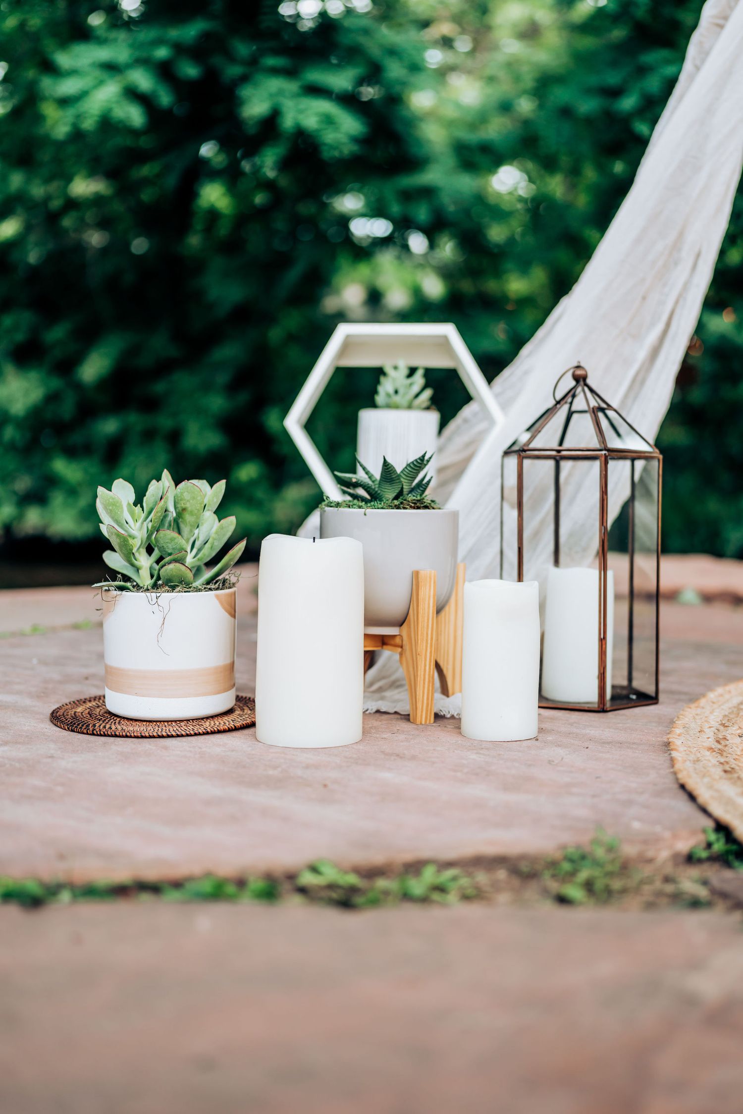 Minimalist wedding decor display with white candles, succulents, and a geometric lantern on a rustic surface.
