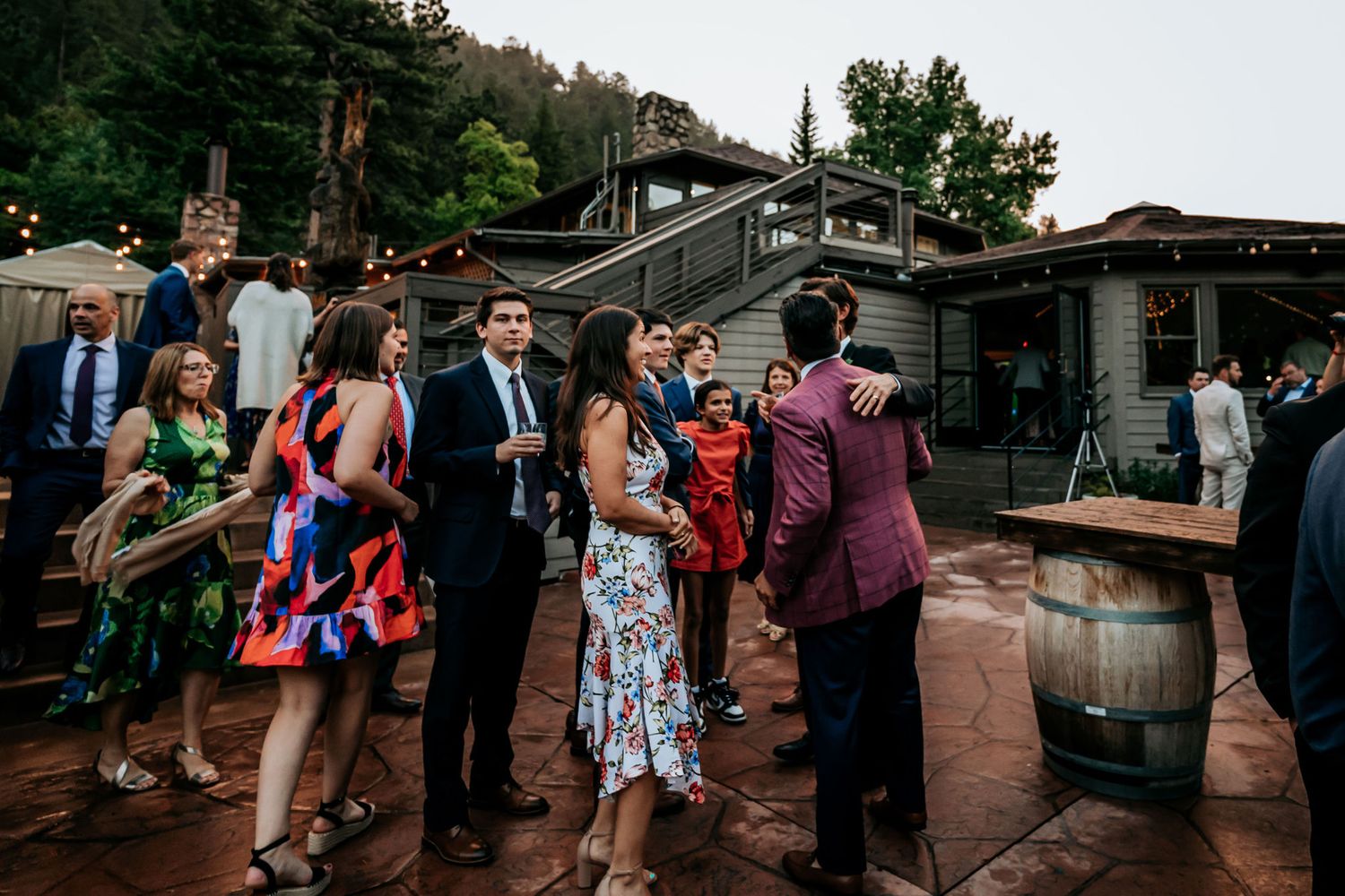 Wedding guests mingle and dance at an outdoor reception venue with rustic wine barrels.