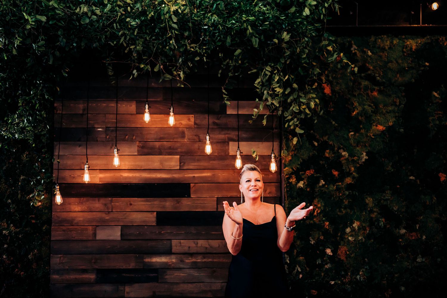 Person in black dress posing dramatically against rustic wooden wall with illuminated decor.
