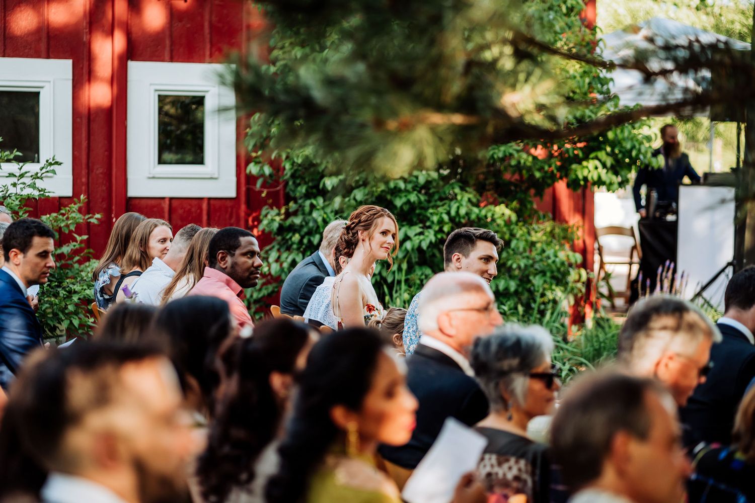 Guests seated at an outdoor event with a red barn visible in the background.