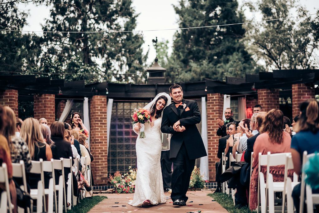 Wedding ceremony exit with guests seated in white chairs along brick-lined outdoor pathway.