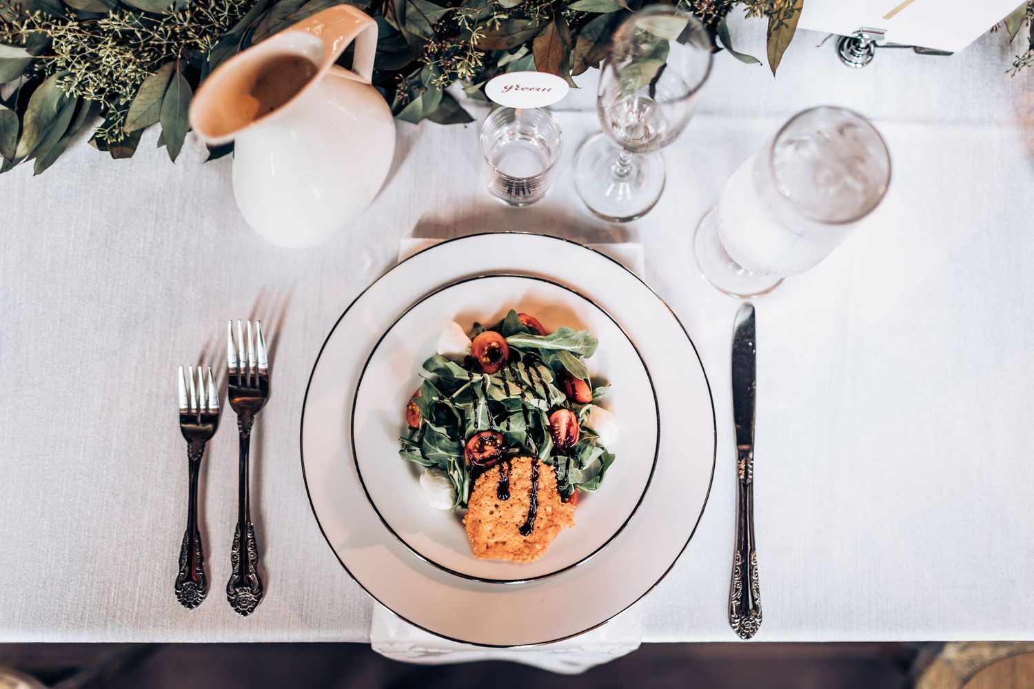 Elegant table setting with plated salmon dish, white china, and decorative greenery garland.