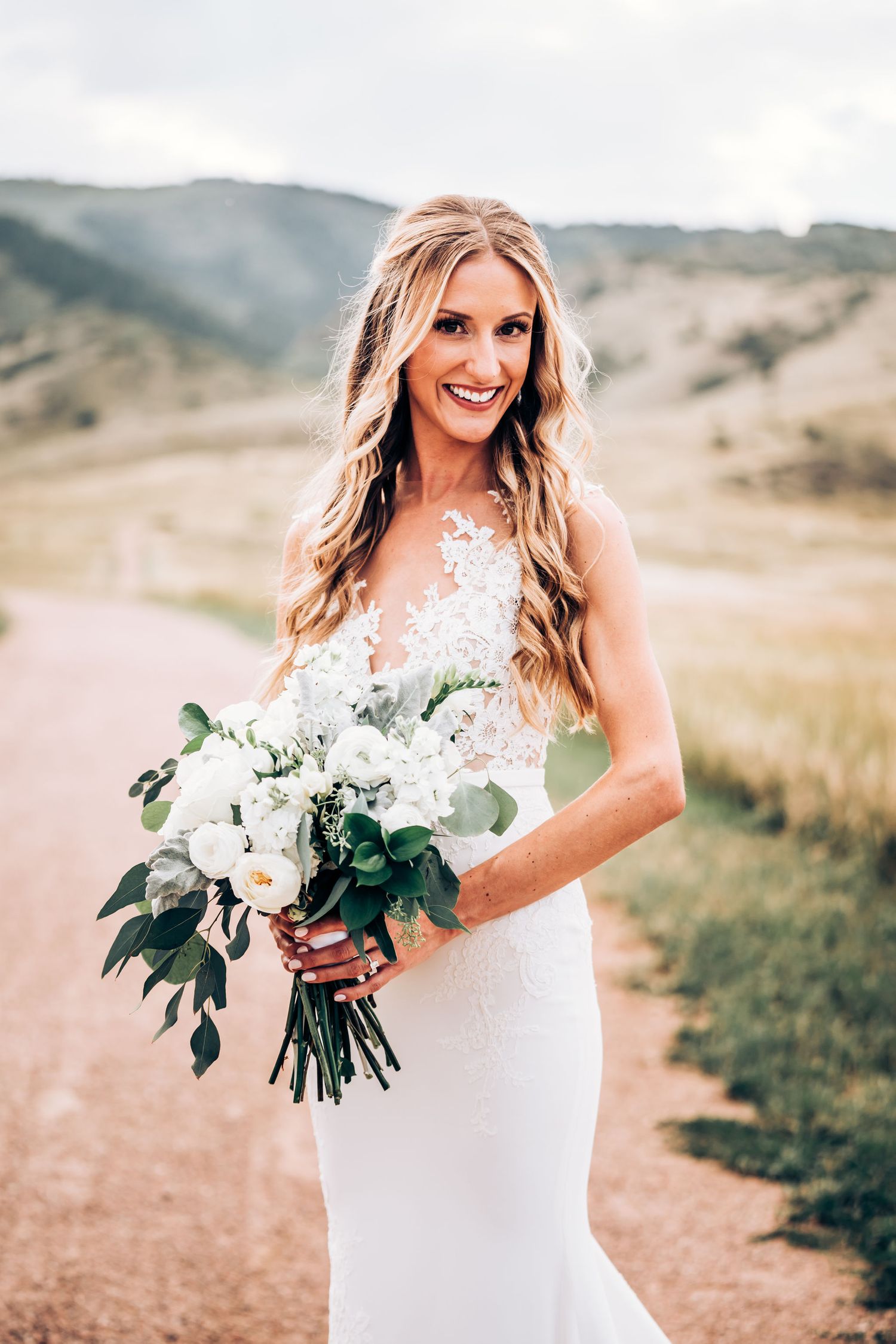 Bridal portrait taken outdoors featuring a white lace wedding gown and natural bouquet in mountain setting.