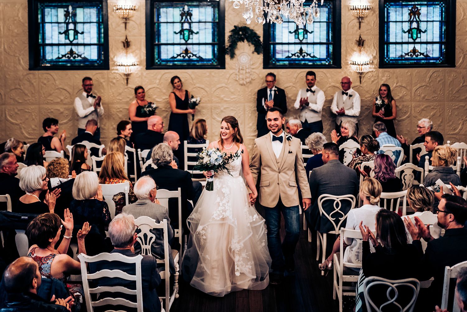 Wedding ceremony in a vintage-style room with four decorative windows and ornate wall details.