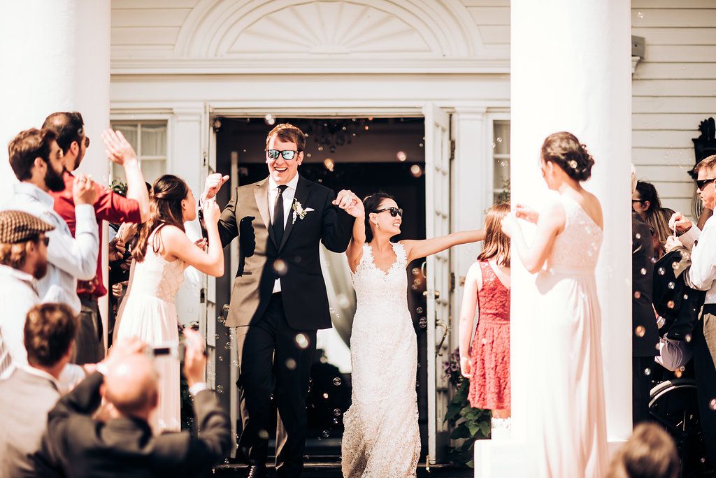 Wedding exit celebration on white columned porch with joyful guests.