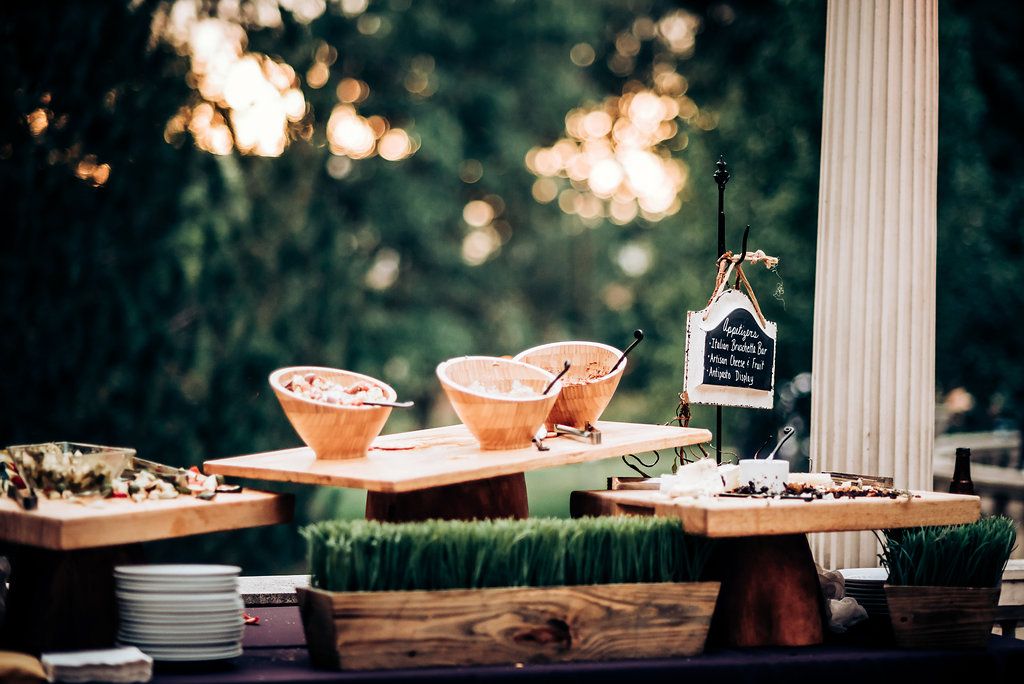 Cocktails and appetizers displayed on rustic wooden table at outdoor event.