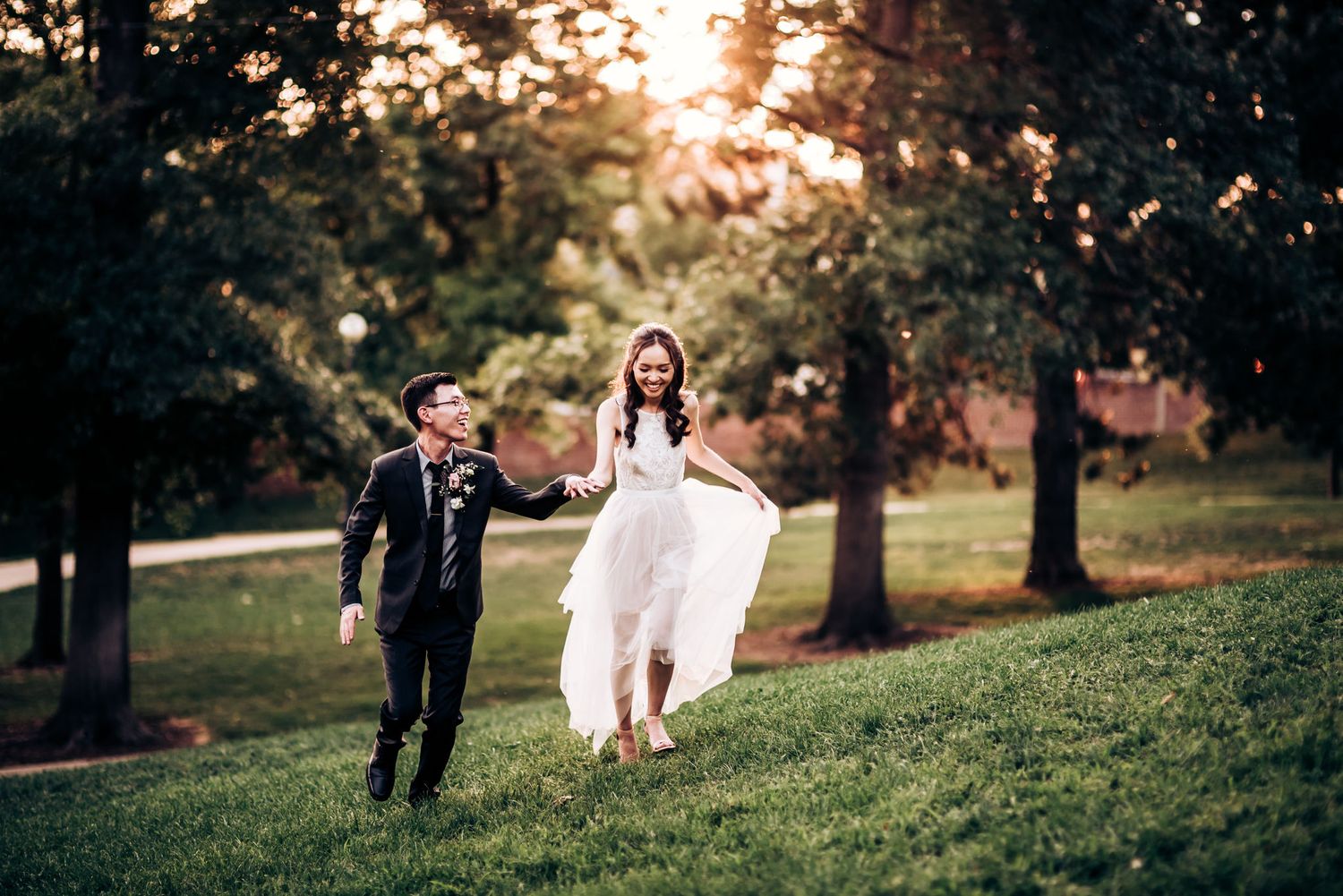 A playful couple runs together on a grassy hill during sunset.