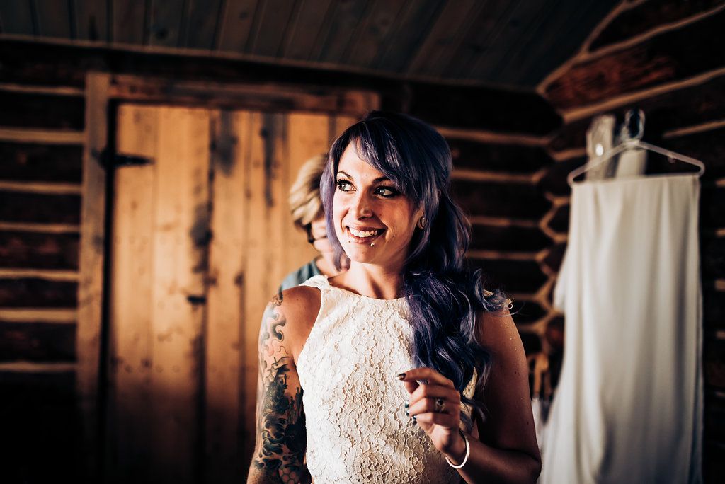 A tattooed woman in a white lace dress smiles while holding a glass.