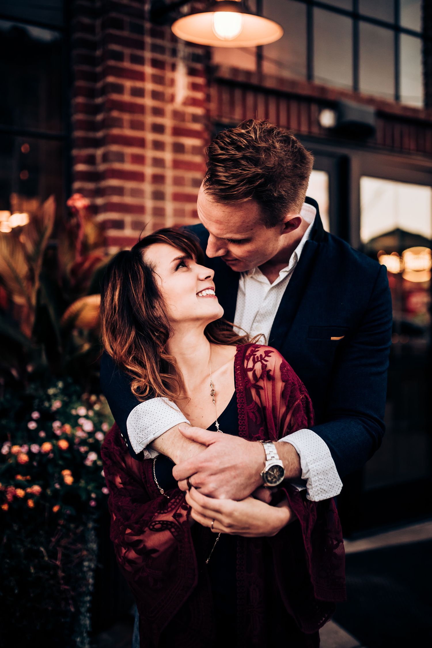 Romantic embrace under warm lighting against industrial brick backdrop.