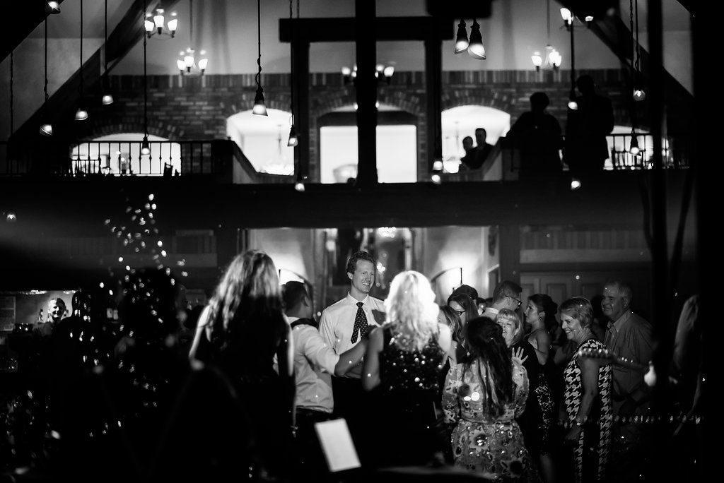 Black and white photo of guests dancing at a dimly lit indoor celebration with crosses and lights.