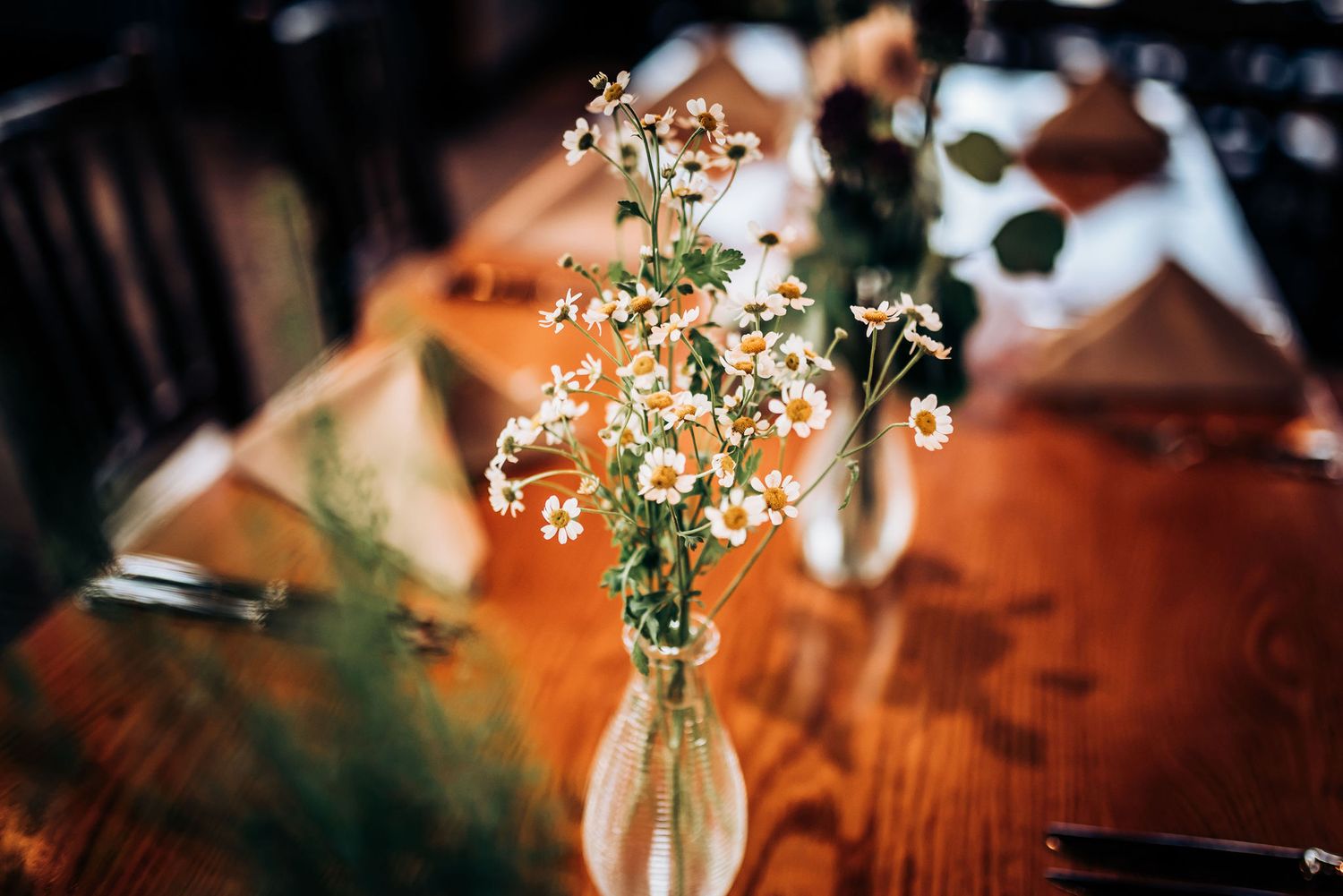 Delicate white flowers in clear glass vase on wooden table with soft ambient lighting.
