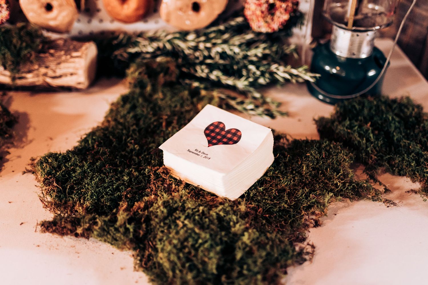 A small gift box with heart decoration sits on a bed of green moss with a lantern in the background.