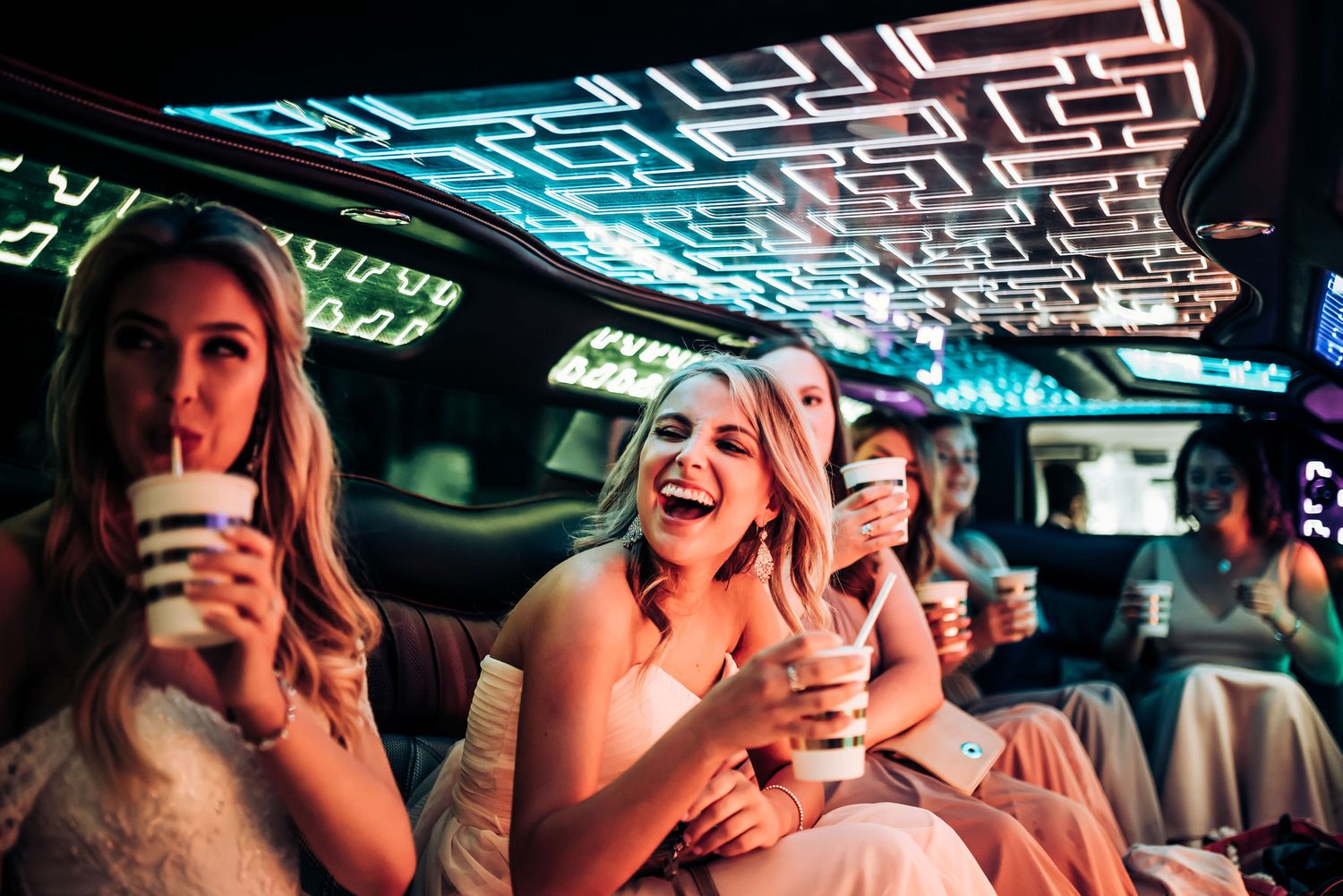 Friends celebrating in a party limo with drinks under neon blue ceiling lights.