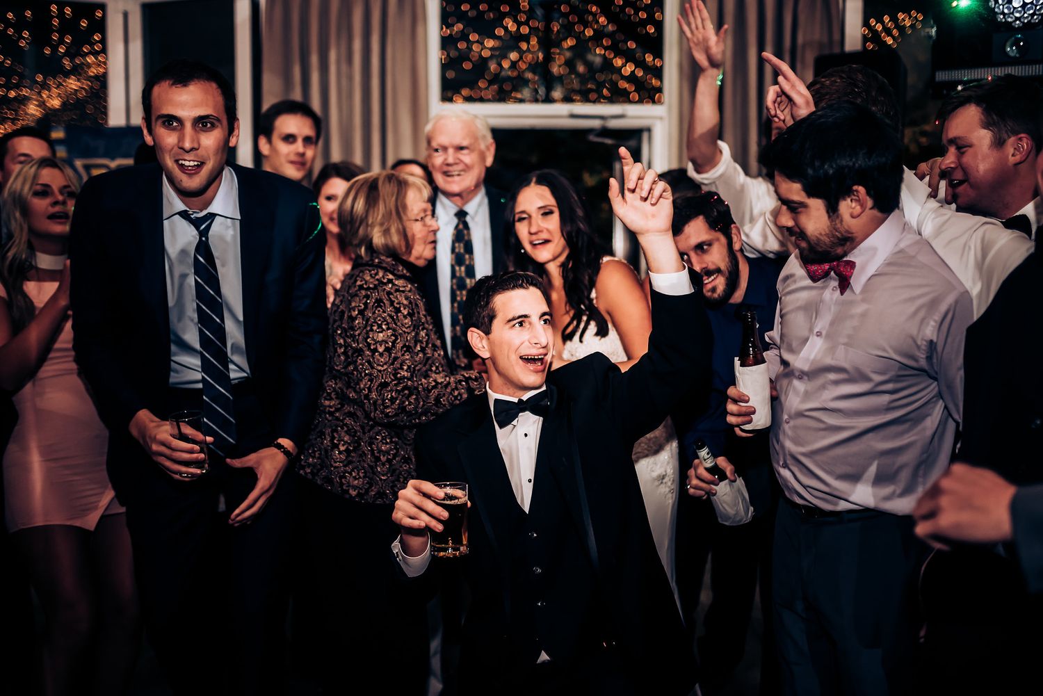 Celebration guests dance and socialize on a packed dance floor under string lights.
