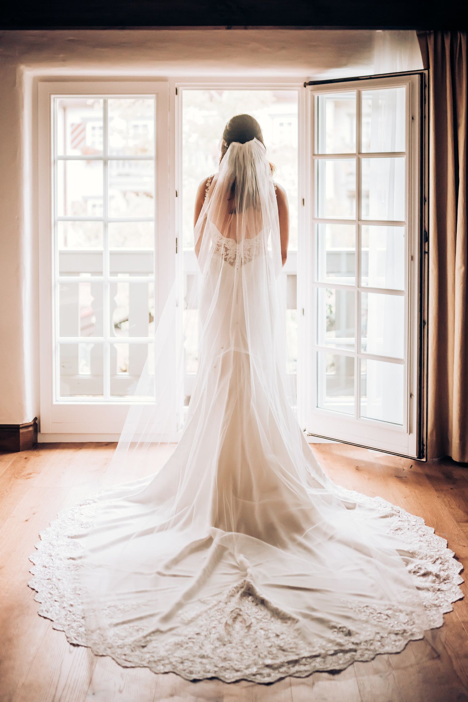Stunning back view of a lace-trimmed wedding gown and veil against French doors.
