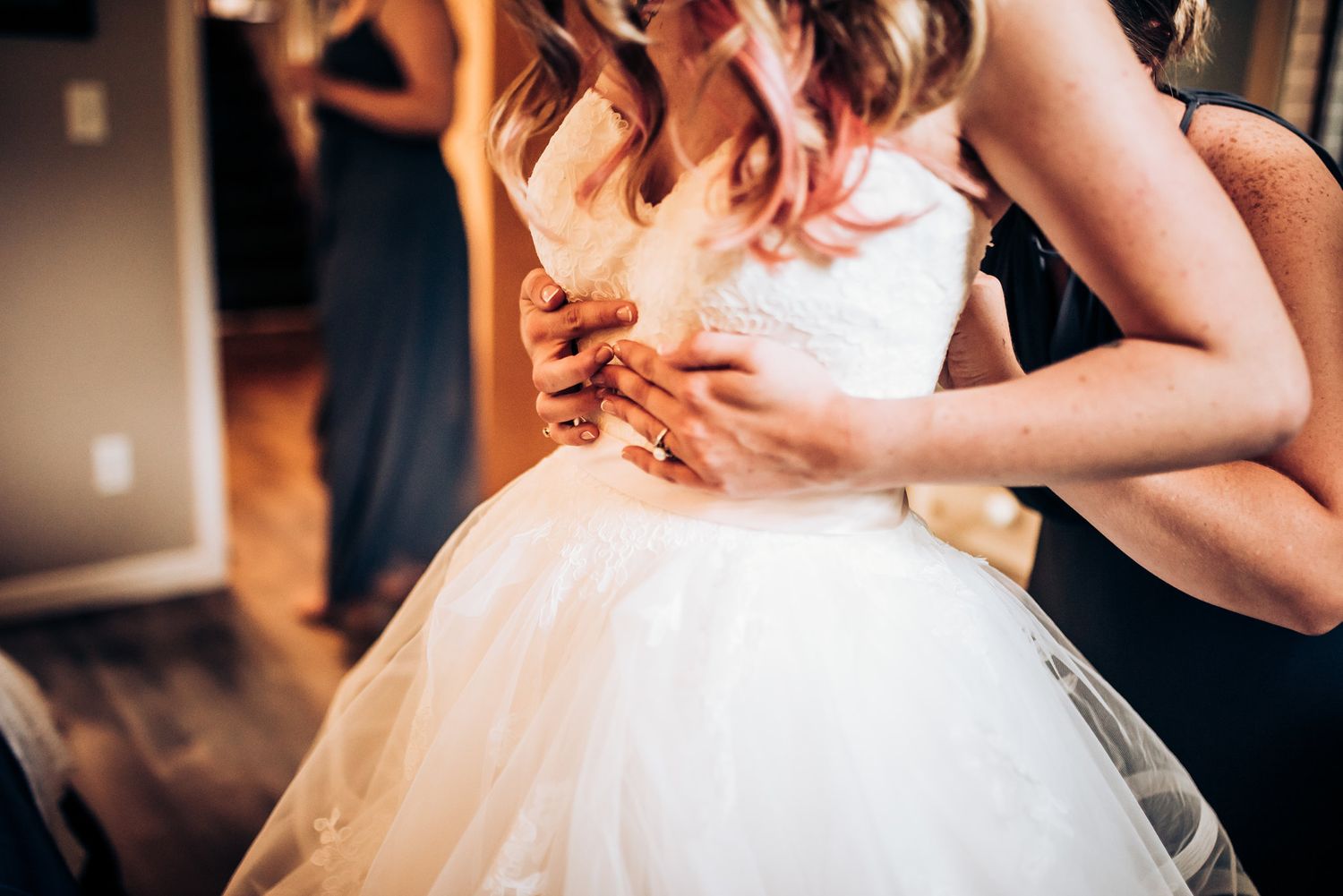 Hands helping adjust the bodice of a white tulle wedding gown.